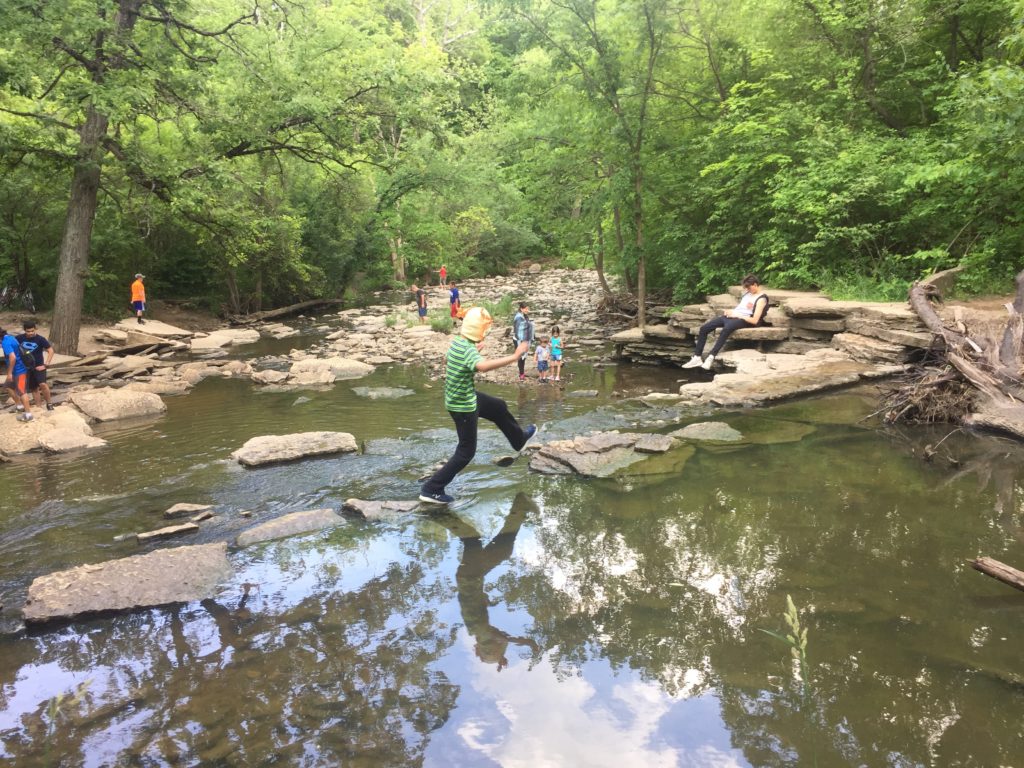 boy using rocks to cross creek above small falls