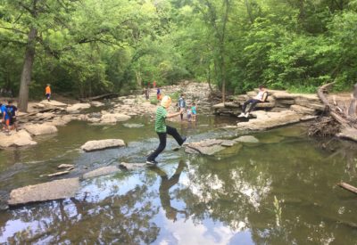 boy using rocks to cross creek above small falls