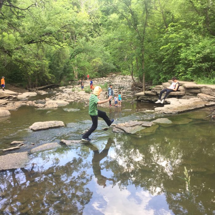 boy using rocks to cross creek above small falls